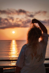 Rear view of woman standing against sea during sunset