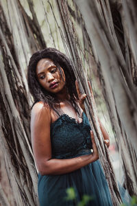 Portrait of smiling woman standing by tree trunk