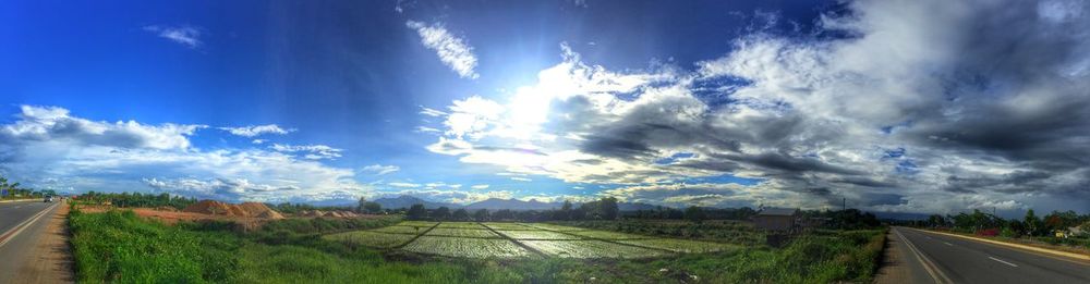 Panoramic view of road by field against sky