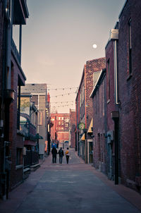 People on road amidst buildings against sky at dusk