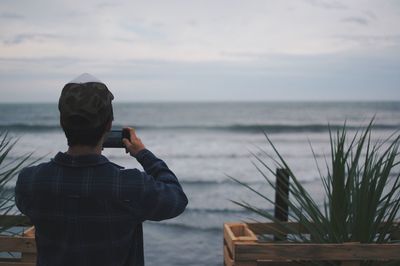 Rear view of man photographing sea from mobile phone