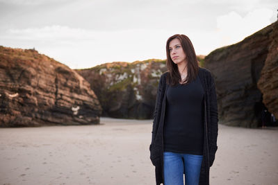 Young woman looking away while standing on land against sky