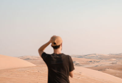 Young man on sand dune in desert against clear sky