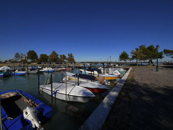 Boats moored at harbor against clear blue sky