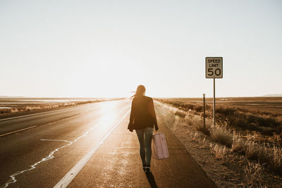 Rear view of woman walking on road against clear sky