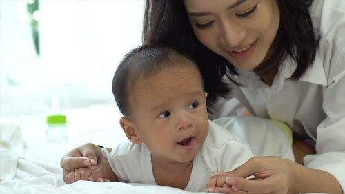 Smiling mother playing with cute baby son on bed at home