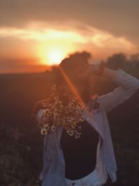 Midsection of woman standing on field against sky during sunset