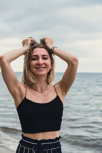 Portrait of young woman standing at beach against sky