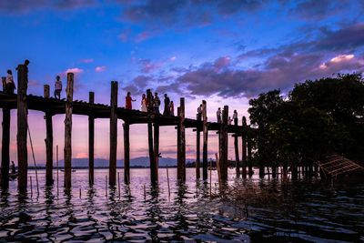 Silhouette wooden posts in sea against sky during sunset