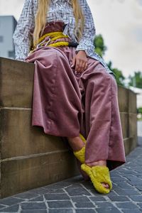 Low section of woman sitting on retaining wall in city