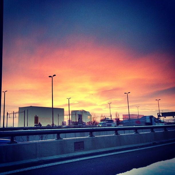 sunset, transportation, car, street light, road, orange color, sky, land vehicle, mode of transport, building exterior, city, architecture, street, built structure, traffic, silhouette, cloud - sky, road marking, dusk, parking lot