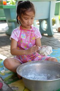 Cute girl preparing dough in container at back yard