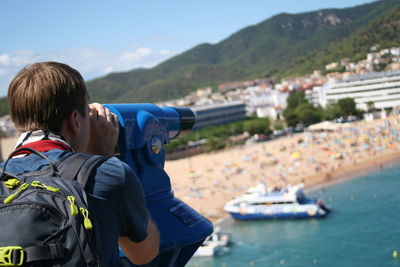 Rear view of man with backpack looking through coin-operated binoculars