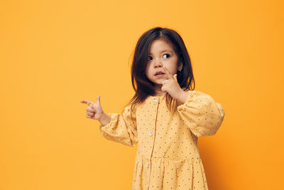 Portrait of young woman standing against yellow background