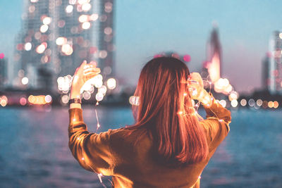 Rear view of woman standing in illuminated city against sky