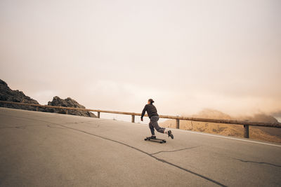 Young man skateboarding on road near railing against sky