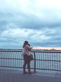 Woman photographing while standing by sea against sky