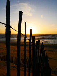 Wooden fence at beach against sky during sunset