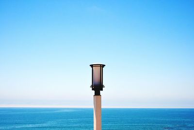 Street light by sea against clear blue sky
