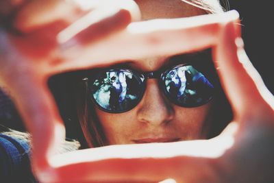 Close-up of woman wearing sunglasses with reflection seen through finger frame