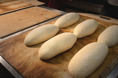 Several raw french rolls lie on a wooden baking sheet in the bakery's bread room before baking in