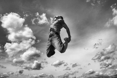 Low angle view of man jumping against cloudy sky