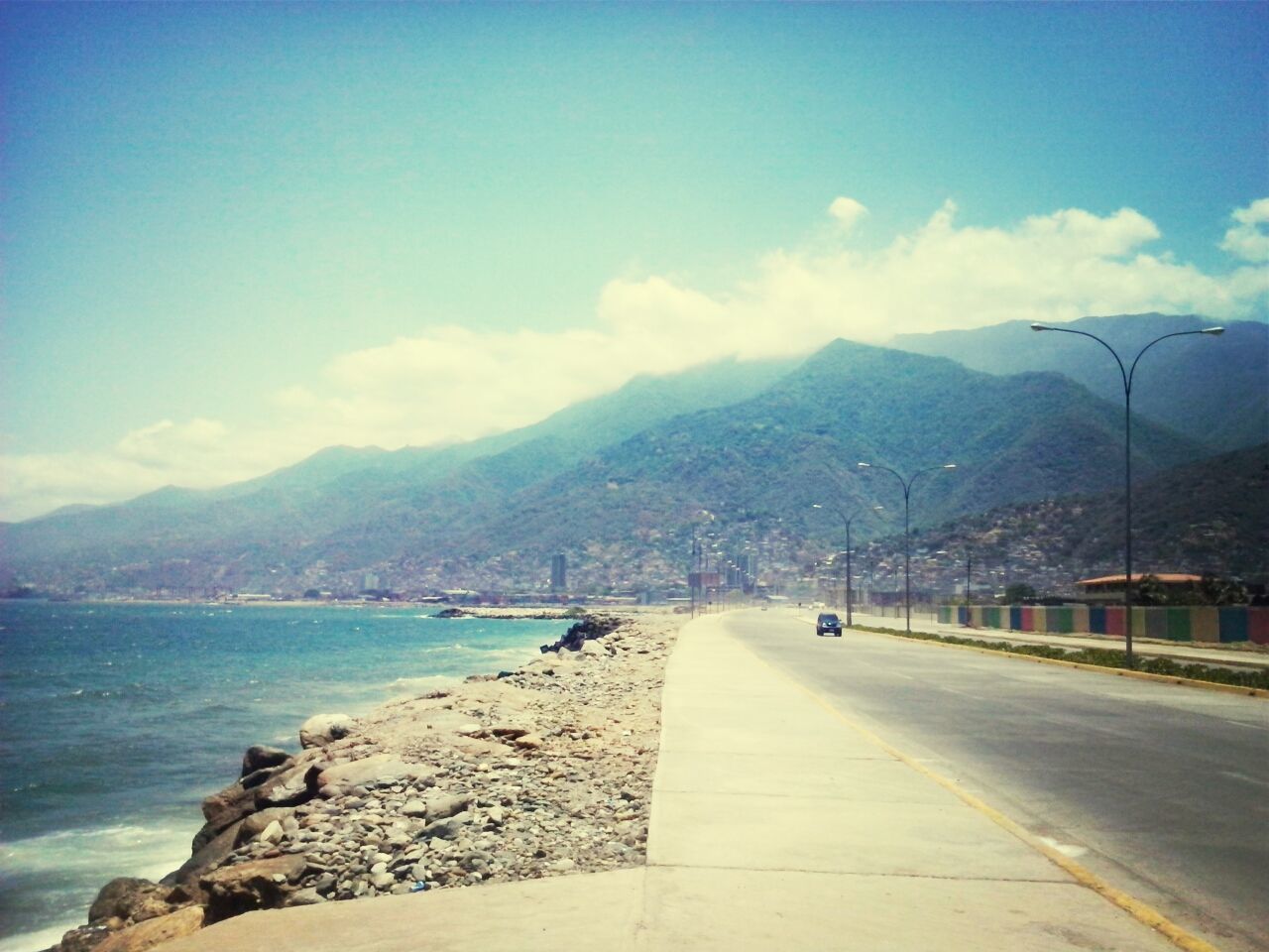 mountain, sky, mountain range, the way forward, water, road, transportation, cloud - sky, scenics, tranquil scene, cloud, tranquility, nature, beauty in nature, sea, road marking, railing, street, outdoors, diminishing perspective