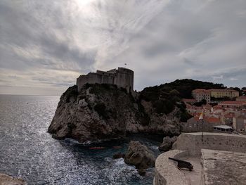 Old building by sea against cloudy sky