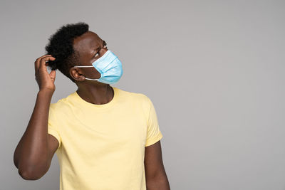 Afro-american man wear face mask, scratches her head and thinks, looking up at blank copy space 