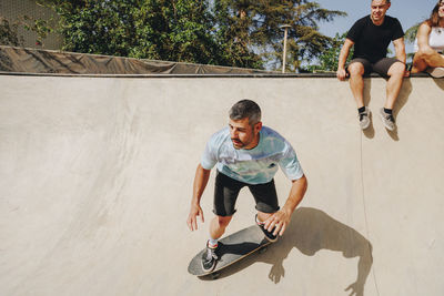 Man skateboarding on sports ramp with friends in background