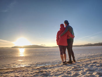 Sports couple hold hands on hips at bank of frozen pond, guy and girl in winter training clothes