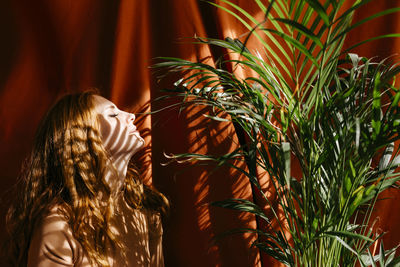 Shadow of leaves falling on woman's face by red backdrop