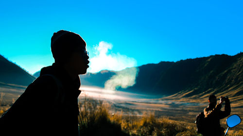 Silhouette man standing on mountain against blue sky