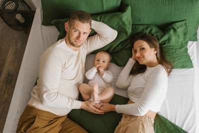 Young happy parents spend time with their little child son lying on a cozy bed