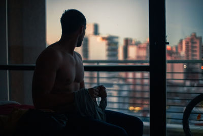 Shirtless man looking through window at home