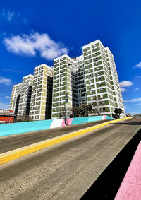 Road by buildings against blue sky in city