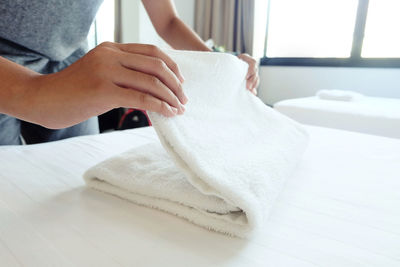 Midsection of woman folding towel on bed at home