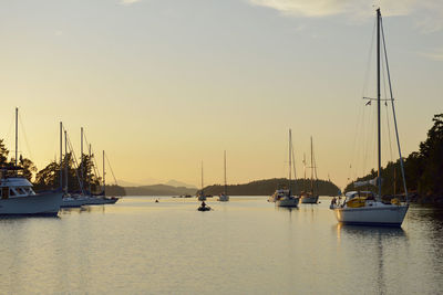 Sailboats moored in harbor against sky during sunset