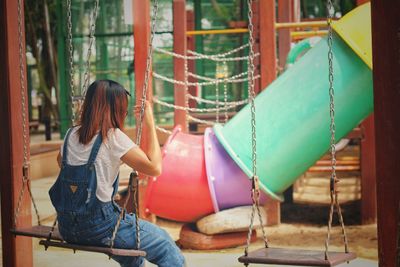 Rear view of woman sitting on swing in playground