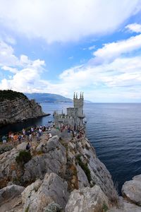 Group of people on rock by sea against sky