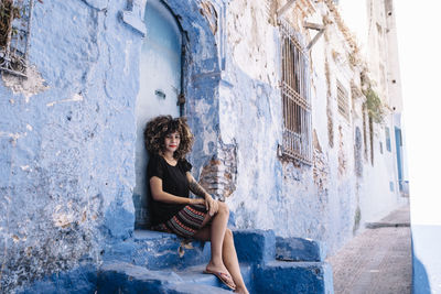 Portrait of young woman sitting by old house