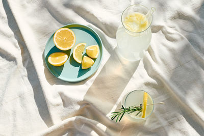 Summer refreshing lemonade drink or alcoholic cocktail with ice, rosemary and lemon slices on table