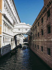 Canal amidst buildings against blue sky in city during sunny day