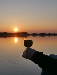 Close-up of hand holding sun shining over river during sunset