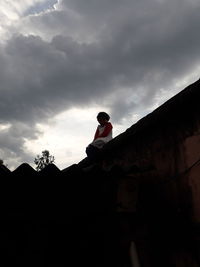 Low angle view of man standing by building against sky