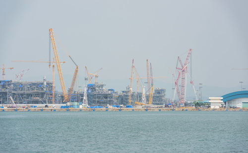 Cranes at harbor against clear sky