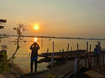 Rear view of woman standing by sea against sky during sunset