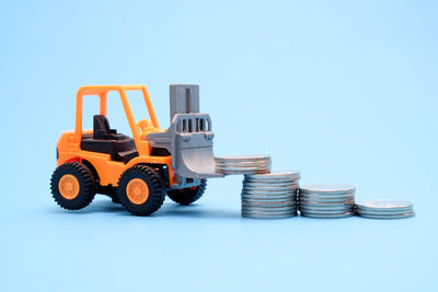 Close-up of toy tractor stacking coins against blue background