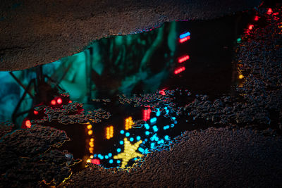 Lights of a fairground ride reflected in a puddle of rainwater at night. 