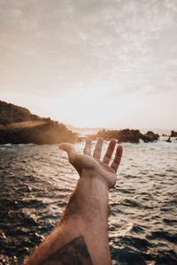 Person hand by sea against sky